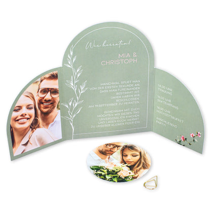 Geöffnete Hochzeitseinladung auf weißem Hintergrund mit Foto, Wunschtext, Ablaufplan und rundem Fotoanhänger