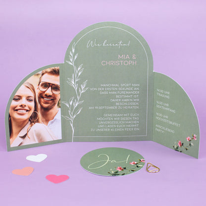 Geöffnete Hochzeitskarte mit Ja Karte, personalisiertem Einladungstext, floralen Elementen und goldener Klammer