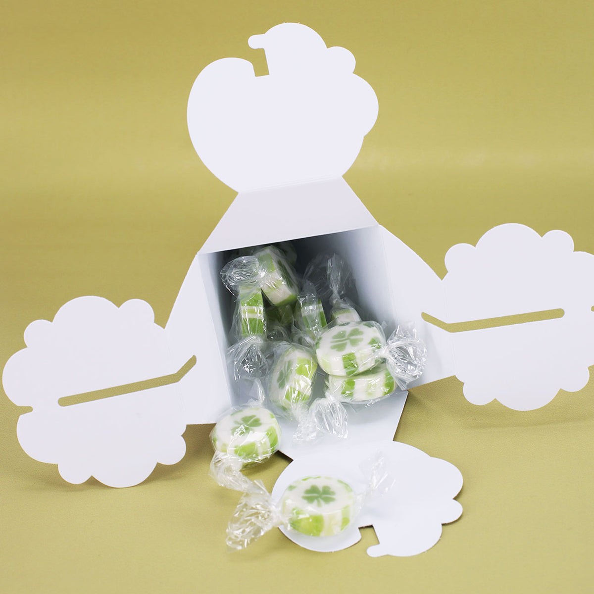 Geöffnete Mini-Schultüte mit Kleeblatt-Bonbons auf hellem Hintergrund