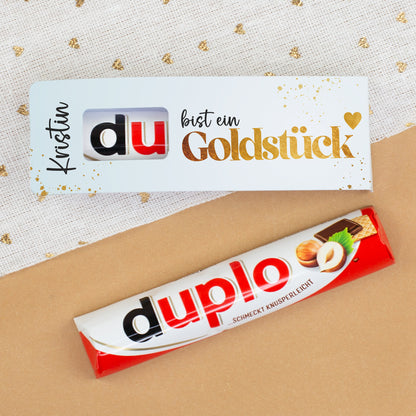 duplo Riegel und Geschenkverpackung mit Goldstück Design auf dekorativem Hintergrund