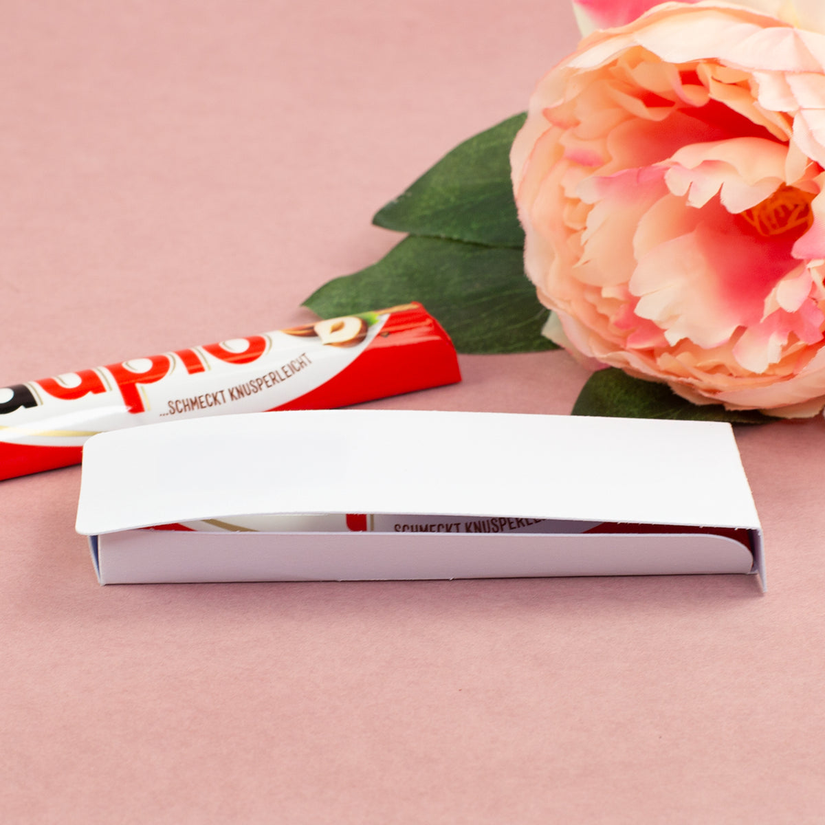 Geöffnete Geschenkverpackung für duplo Riegel mit weißer Innenlasche, Schokoriegel und dekorativer Blume