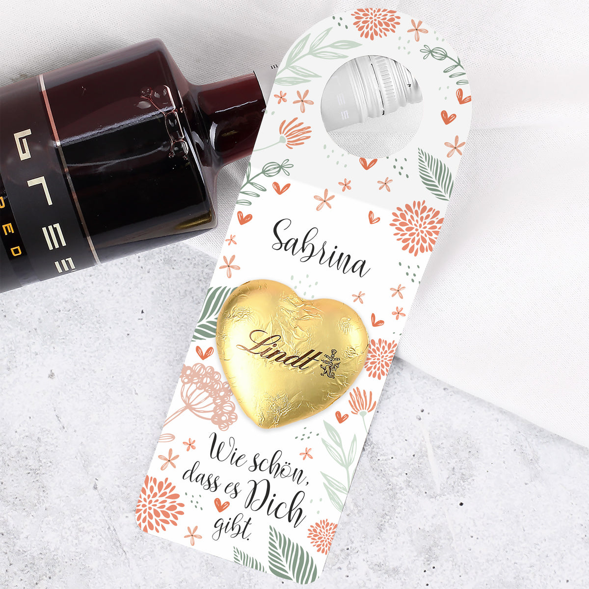 Goldenes Lindt Schokoladenherz auf dem Papieranhänger, hochwertig aufgeklebt und mittig platziert.