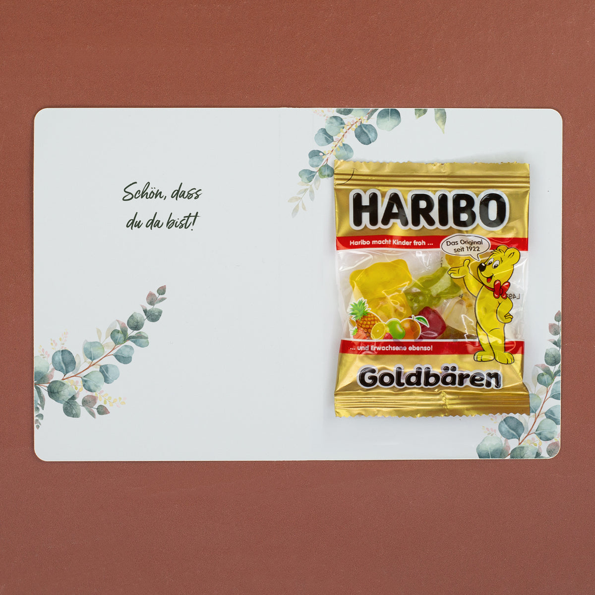 Geöffnetes Gastgeschenk zur Hochzeit mit Innentext „Schön, dass du da bist!“ und Haribo Goldbären