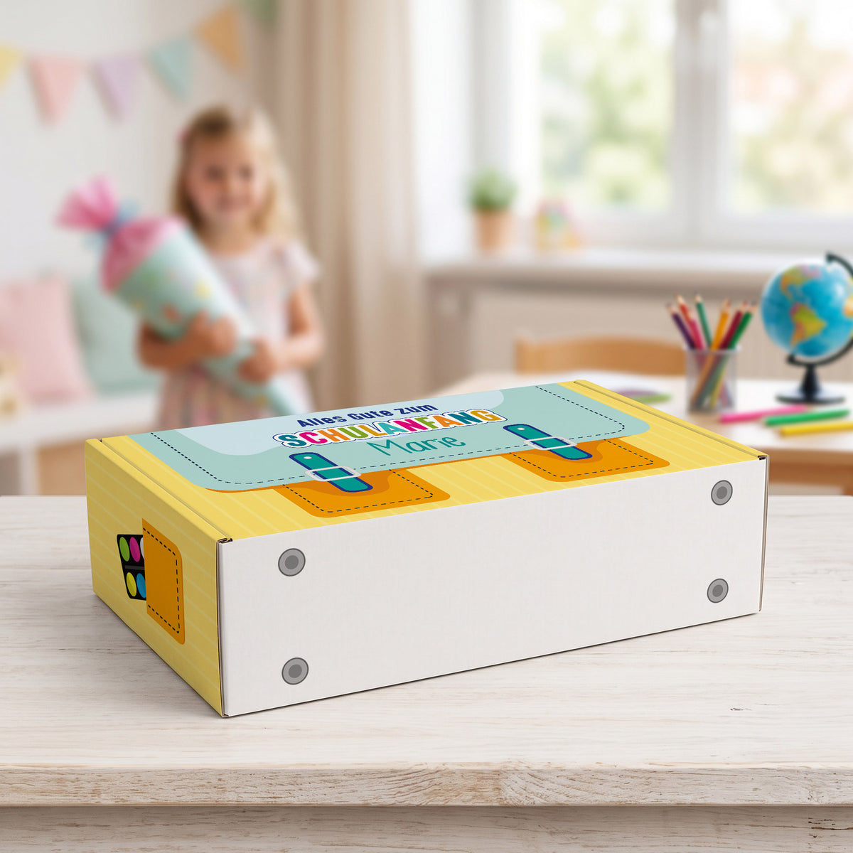 mittlere gelbe Geschenkverpackung liegend auf einen Tisch mit Schulkind im Hintergrund. Bedruckt mit Schulranzen-Motiv und Wunschnamen