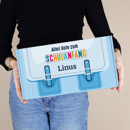 Mittlere personalisierte Aufbewahrungsbox aus Pappe zur Einschulung in Blau mit Schulranzen-Design und Wunschname, von einer Person gehalten