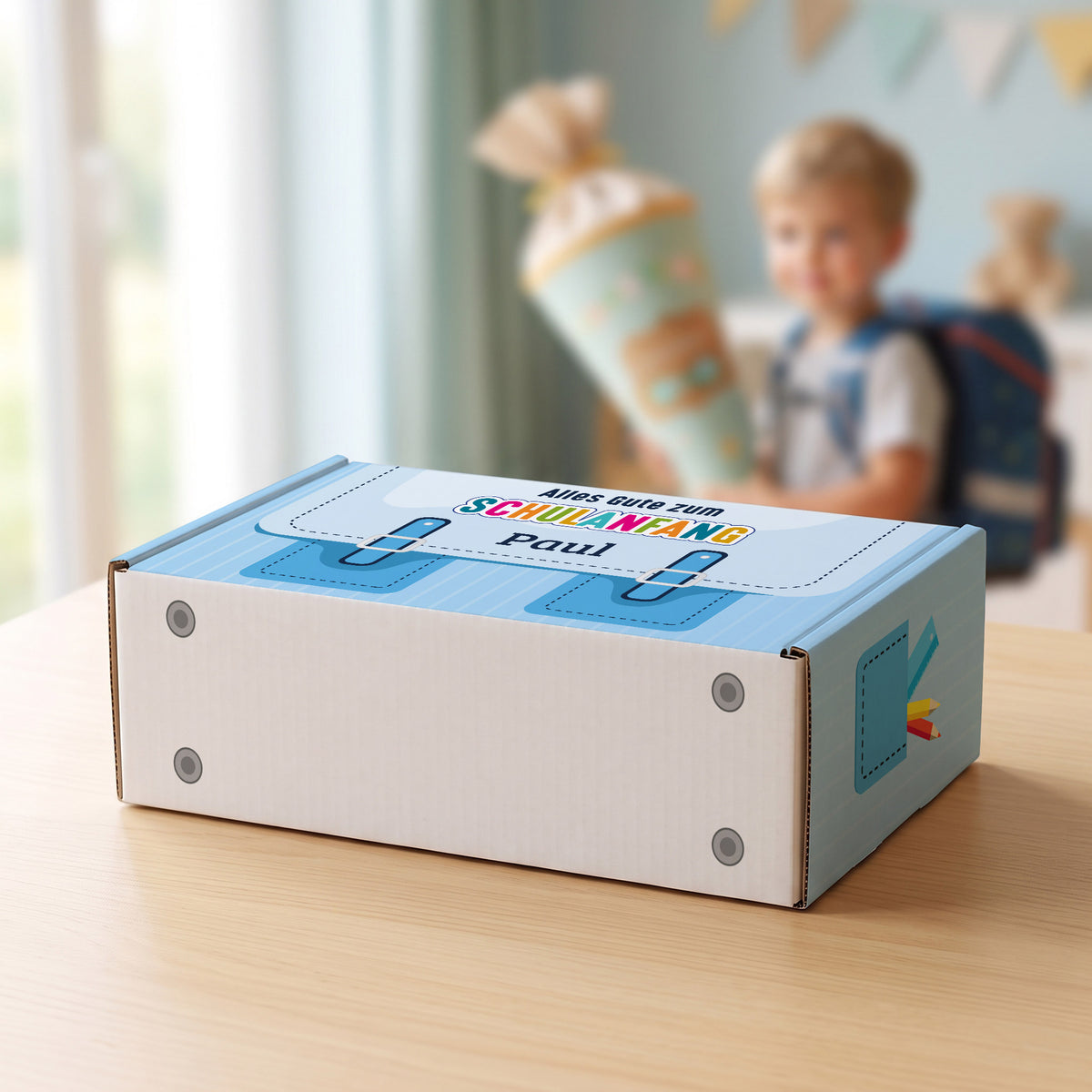 Mittlere blaue Geschenkverpackung zur Einschulung mit Wunschname und Schulkind im Hintergrund