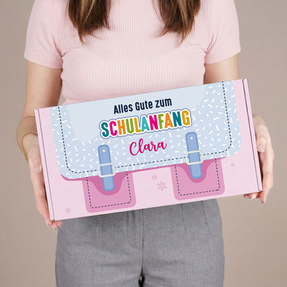 Mittlere personalisierte Pappbox zur Einschulung in Rosa mit Schulranzen-Motiv und Name, in den Händen einer Person