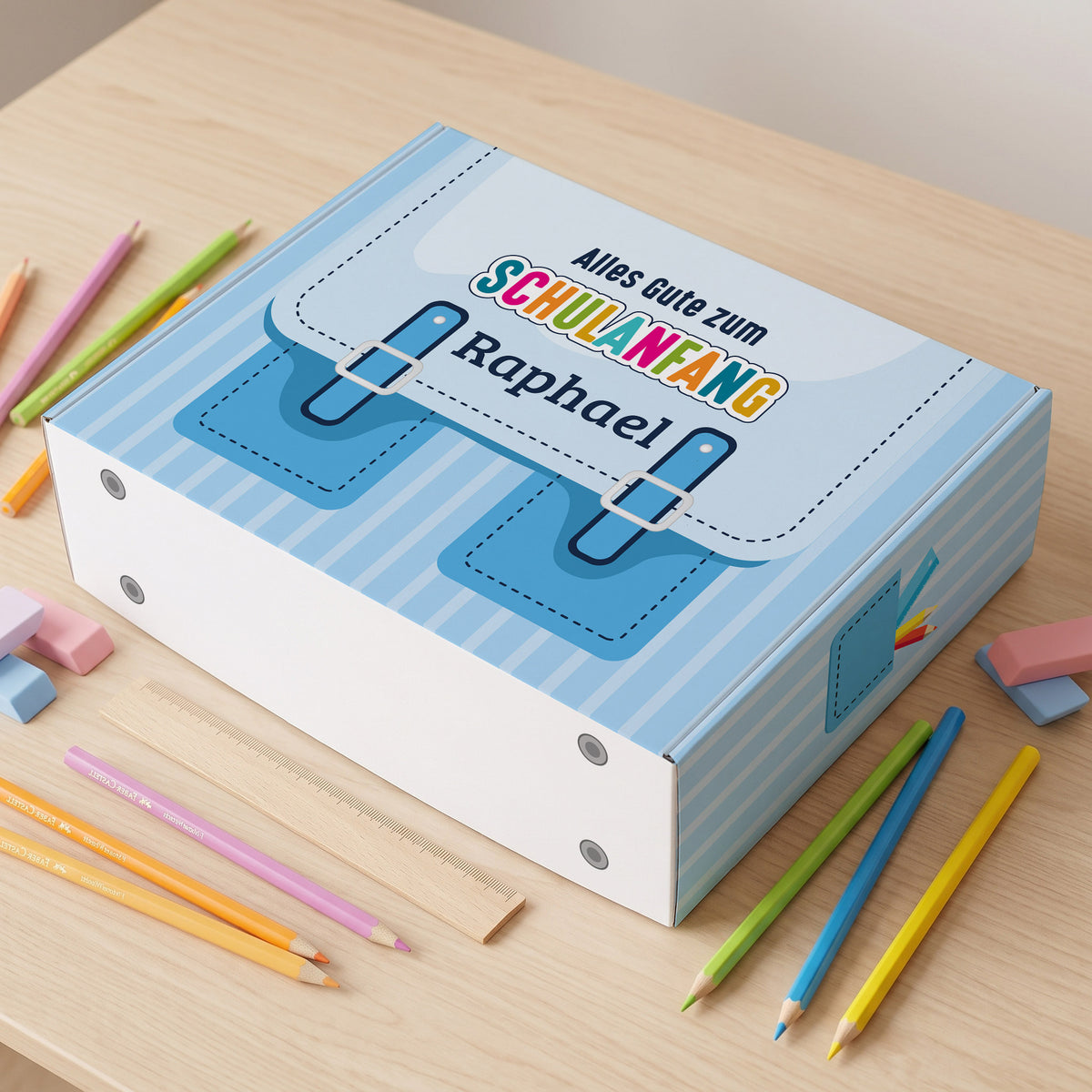 Große blaue Geschenkverpackung zur Einschulung mit Name bedruckt auf einem Schreibtisch liegend
