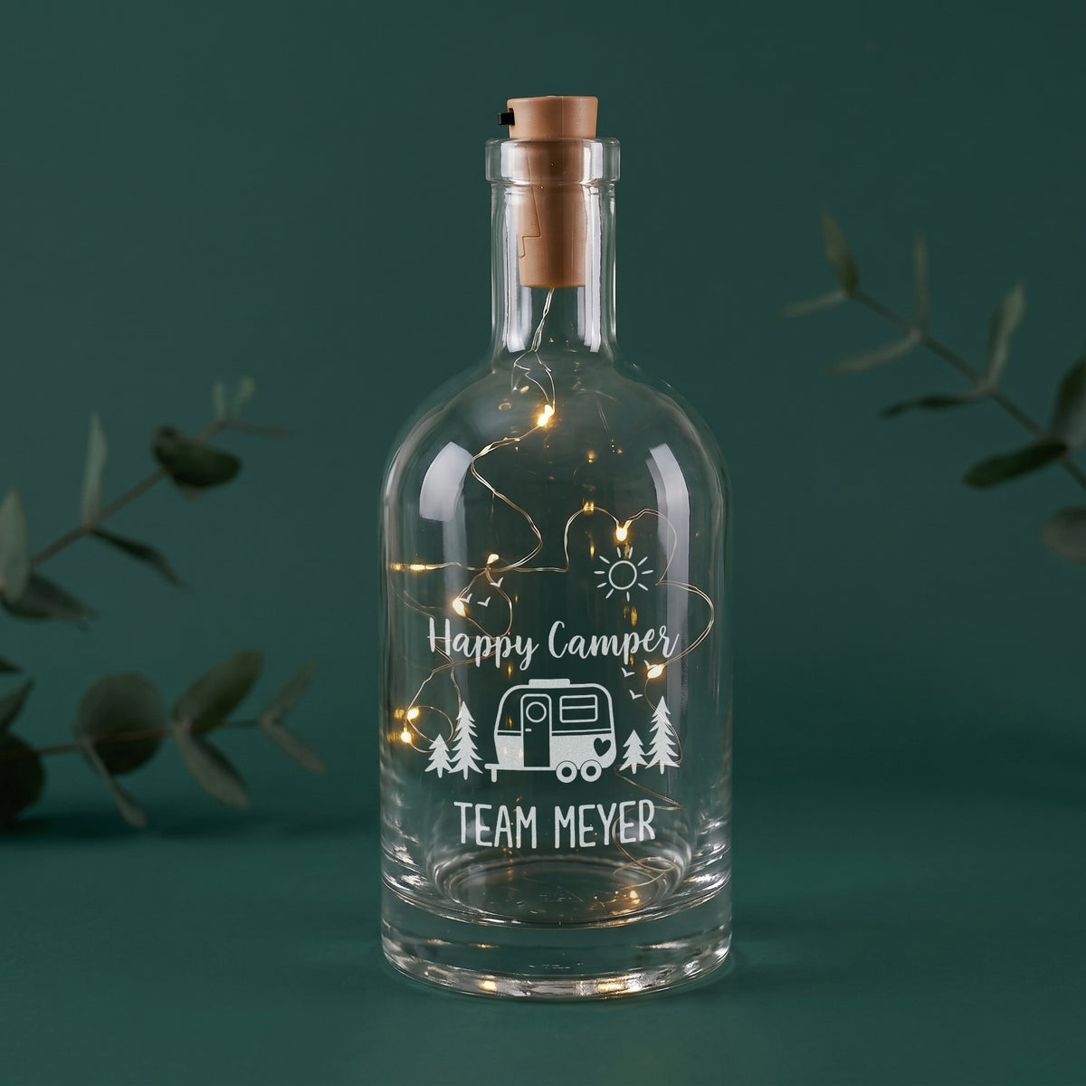 LED-Flaschenlicht aus Glas mit Happy Camper Motiv, Wohnwagen und Wunschtext Team Meyer auf grünem Hintergrund