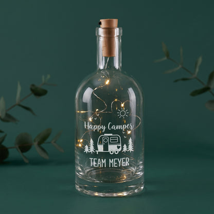LED-Flaschenlicht aus Glas mit Happy Camper Motiv, Wohnwagen und Wunschtext Team Meyer auf grünem Hintergrund