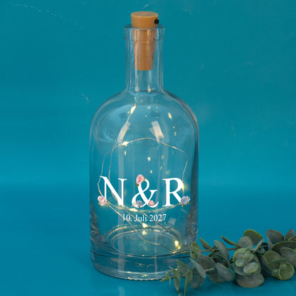 LED-Flasche mit Initialen N & R und Datum 10. Juli 2027, vor türkisfarbenem Hintergrund mit Eukalyptus