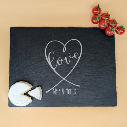Schieferplatte mit Gravur „love“ in Herzform und „Nele & Marius“, dekoriert mit Camembert und Tomaten – auf beigem Hintergrund
