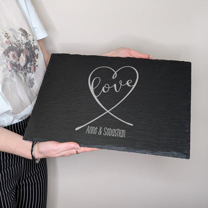 Schieferplatte mit Gravur „love“ in Herzform und „Anne & Sebastian“, von einer Person gehalten zur Größenansicht