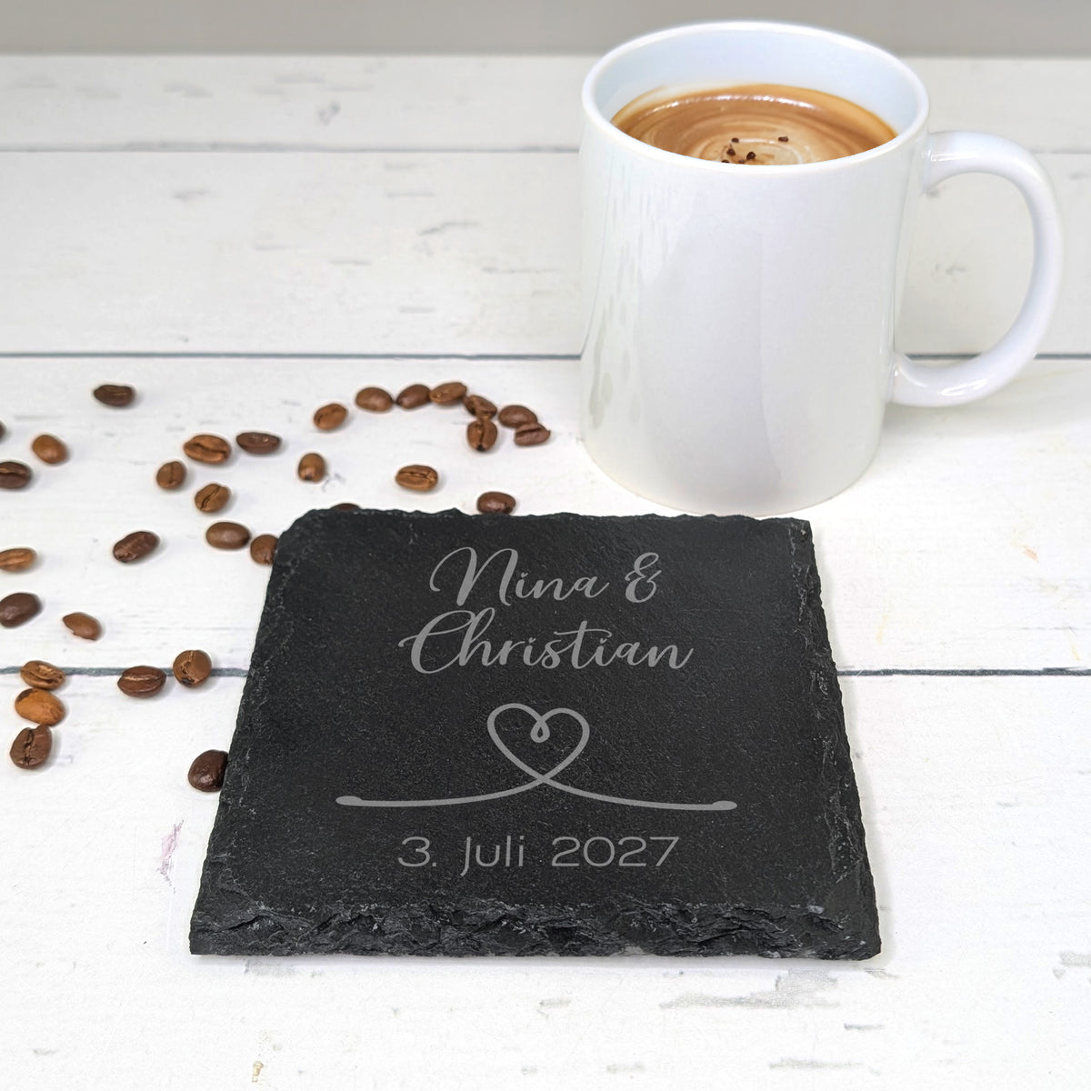 Hochzeits-Untersetzer aus Schiefer mit Gravur "Nina & Christian" und Datum, neben Kaffeetasse und Kaffeebohnen