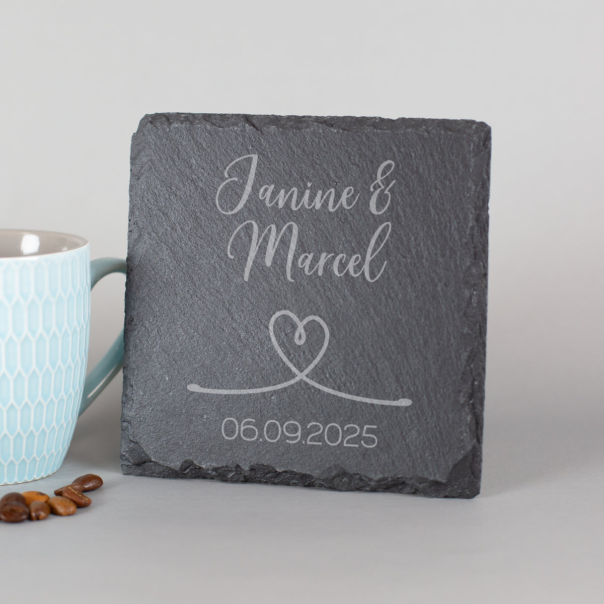 Personalisierter Schiefer-Untersetzer mit Namen und Hochzeitsdatum – angelehnt neben Tasse und Kaffeebohnen