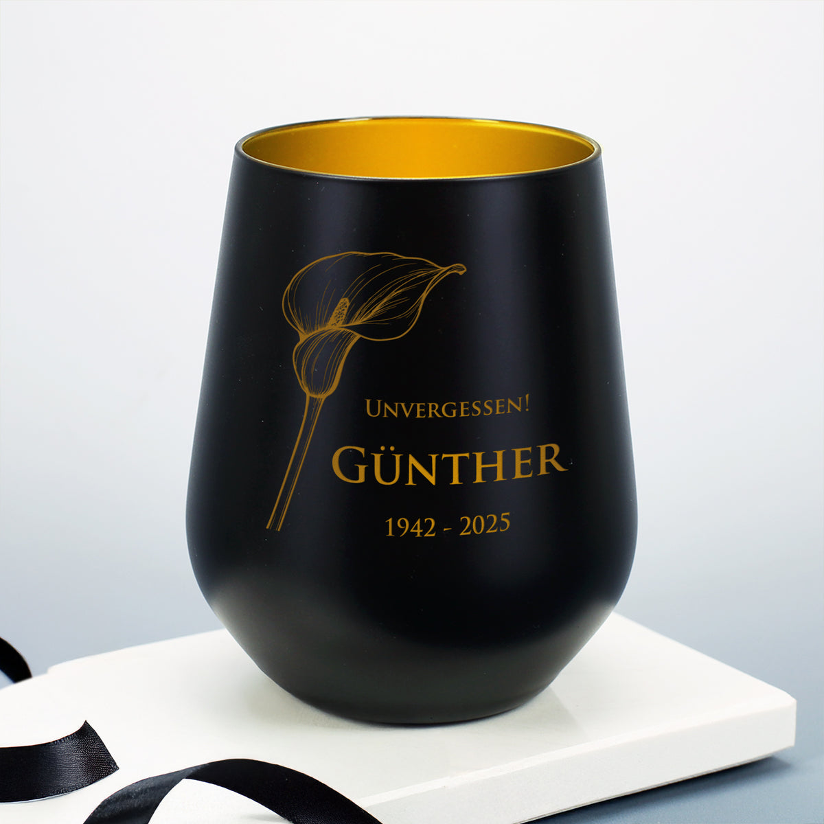 Schwarzes Windlicht mit Calla-Motiv, graviert mit "Unvergessen! Günther 1942–2025", auf weißem Sockel mit Schleifenband