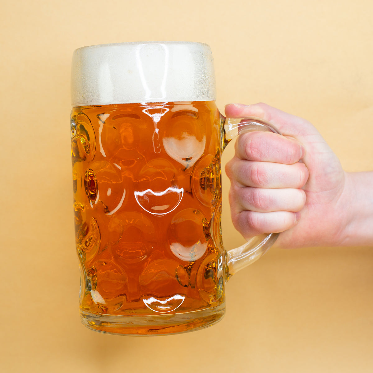 Hand hält großen Bierkrug mit bayerischem Edelweiß-Design – leuchtend bernsteinfarbenes Bier im Glas