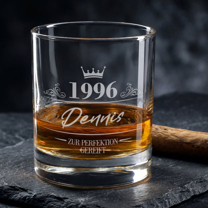 Personalisiertes Whiskyglas zum Geburtstag mit Gravur von 1996, Name Dennis und Krone, gefüllt mit Whisky neben Zigarre