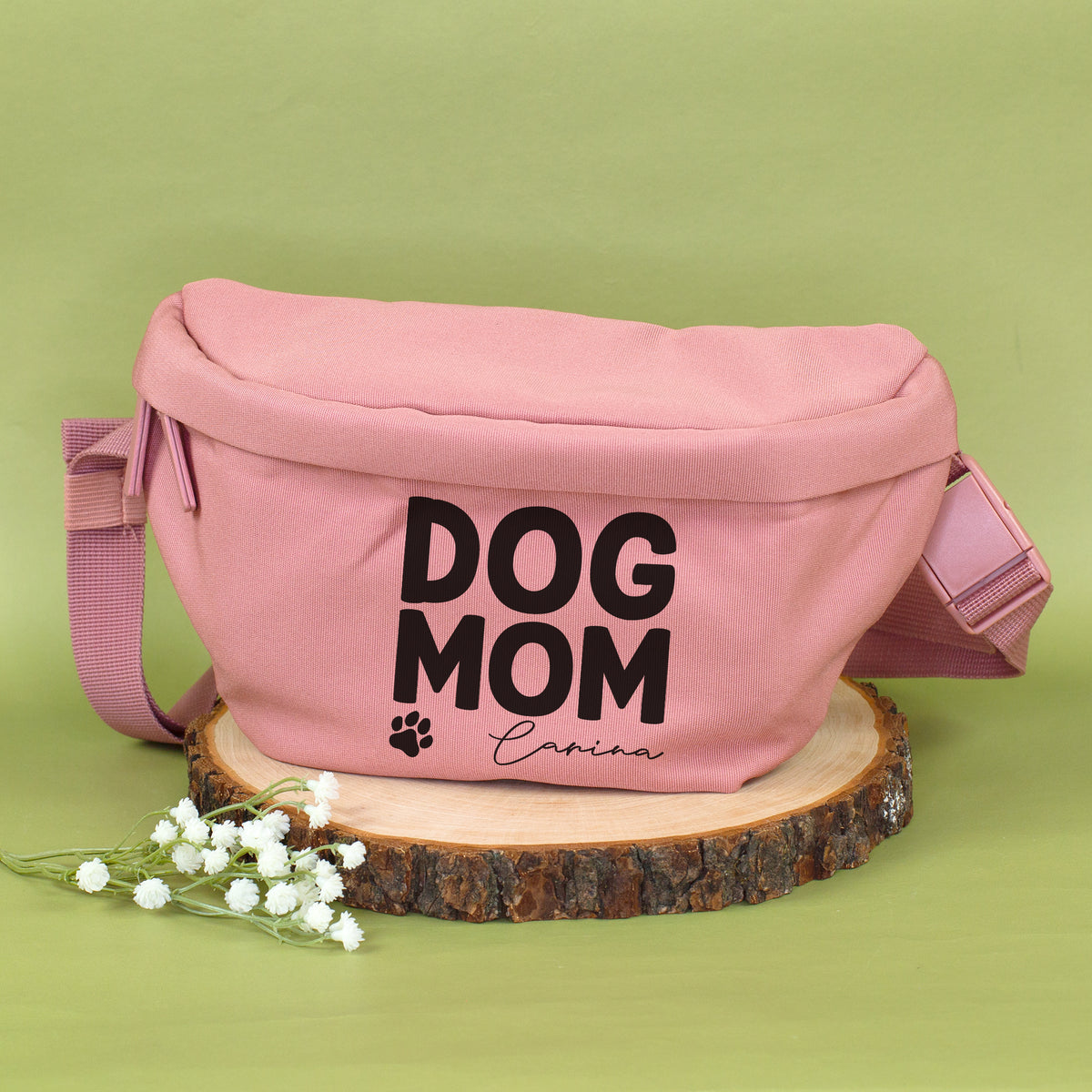Personalisierte rosa Dog Mom Bauchtasche mit Name Carina auf Holzscheibe vor grünem Hintergrund