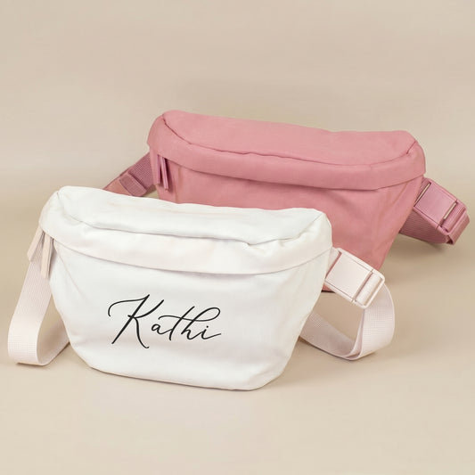 Personalisierte Bauchtaschen in Creme und Rosa mit Namen, Vorderansicht auf beigem Hintergrund