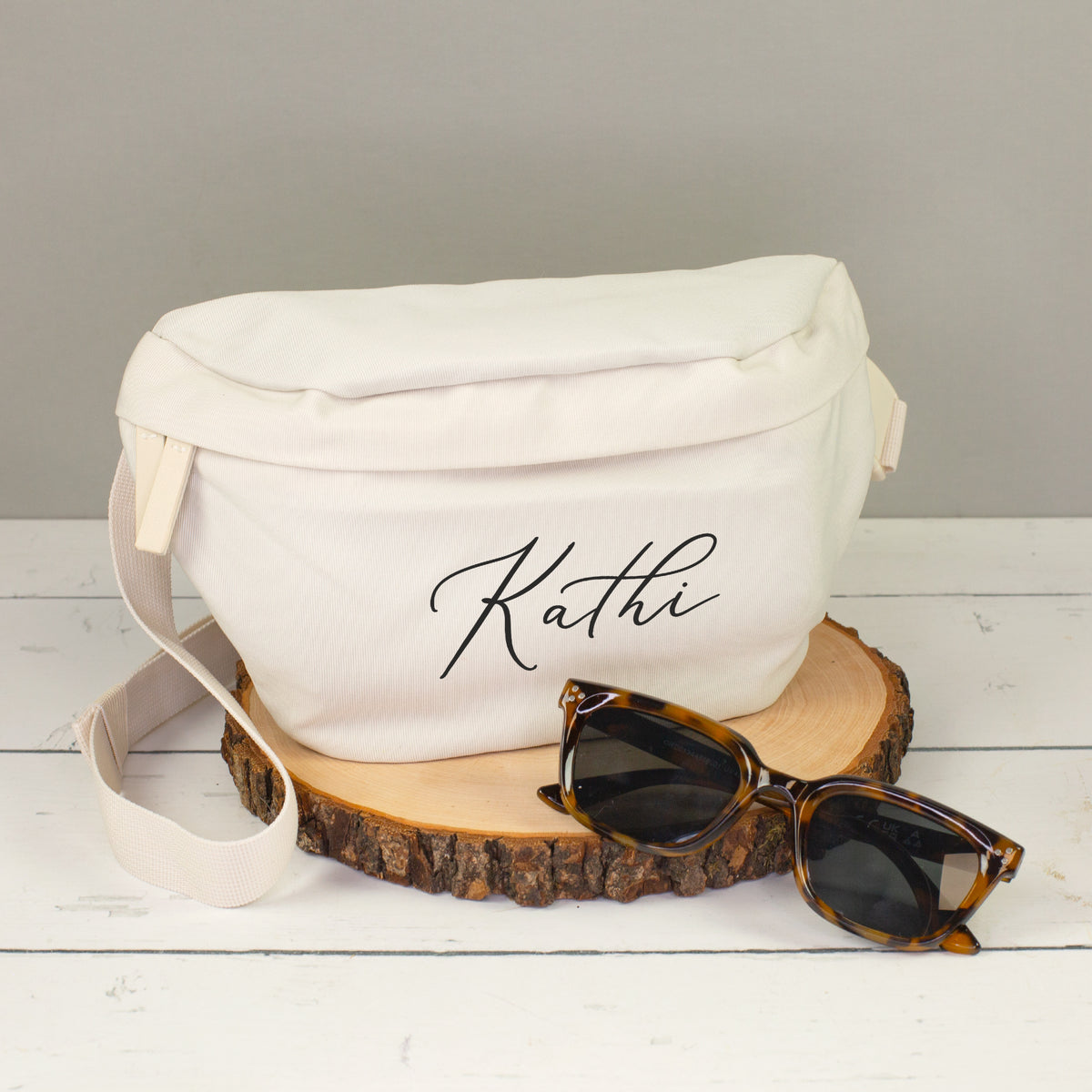 Cremefarbene Bauchtasche mit Name Kathi auf Holzscheibe, dekoriert mit Sonnenbrille