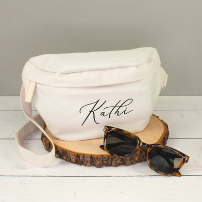 Cremefarbene Bauchtasche mit Name Kathi auf Holzscheibe, dekoriert mit Sonnenbrille