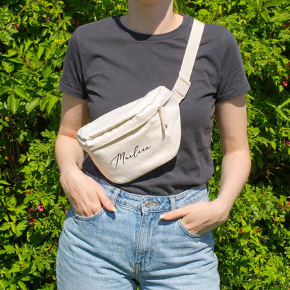 Cremefarbene Bauchtasche mit Name Marleen als Crossbody Bag getragen vor grünem Hintergrund
