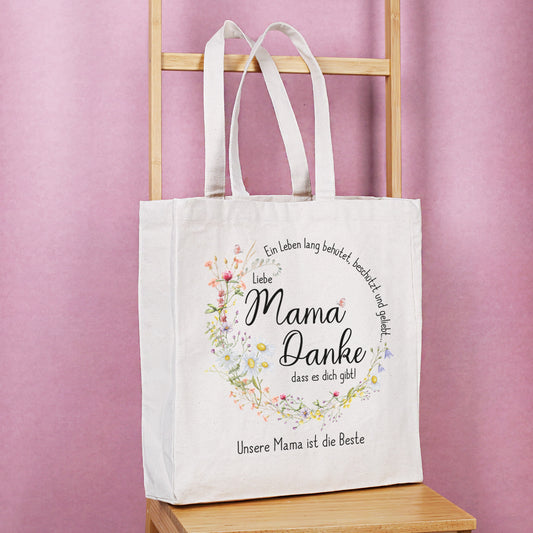 Baumwoll-Einkaufsbeutel mit liebevoller Mama-Botschaft und floralem Kranz, auf einer Holzleiter präsentiert.
