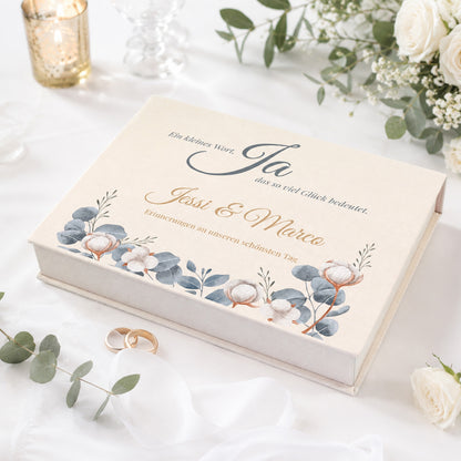 Personalisierte Erinnerungsbox zur Hochzeit mit Eukalyptus-Motiv, Baumwollblüten, Namen und Wunschtext auf festlich gedecktem Tisch