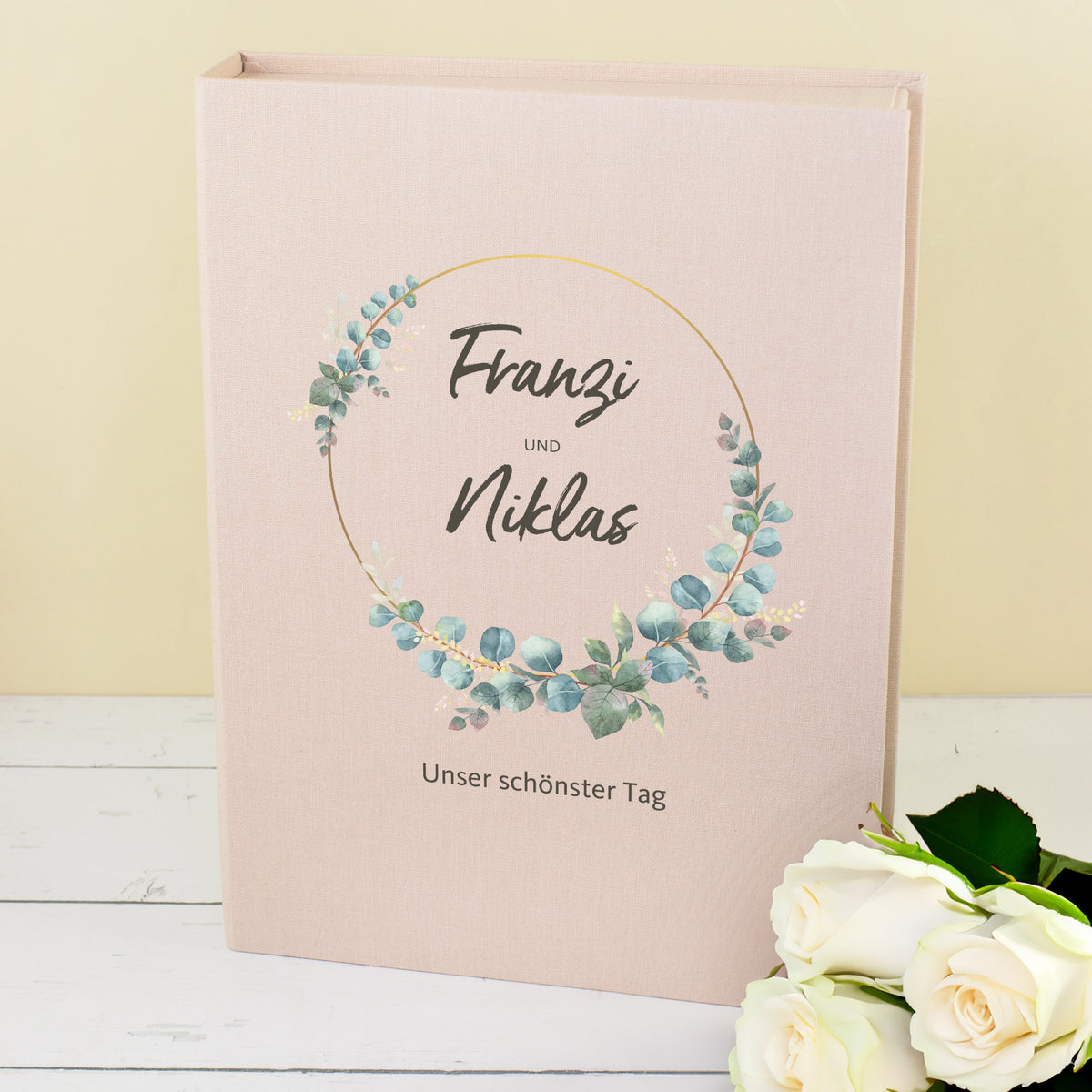 Beige Erinnerungsbox zur Hochzeit mit personalisierten Namen, Eukalyptus-Motiv und Wunschtext neben weißen Rosen