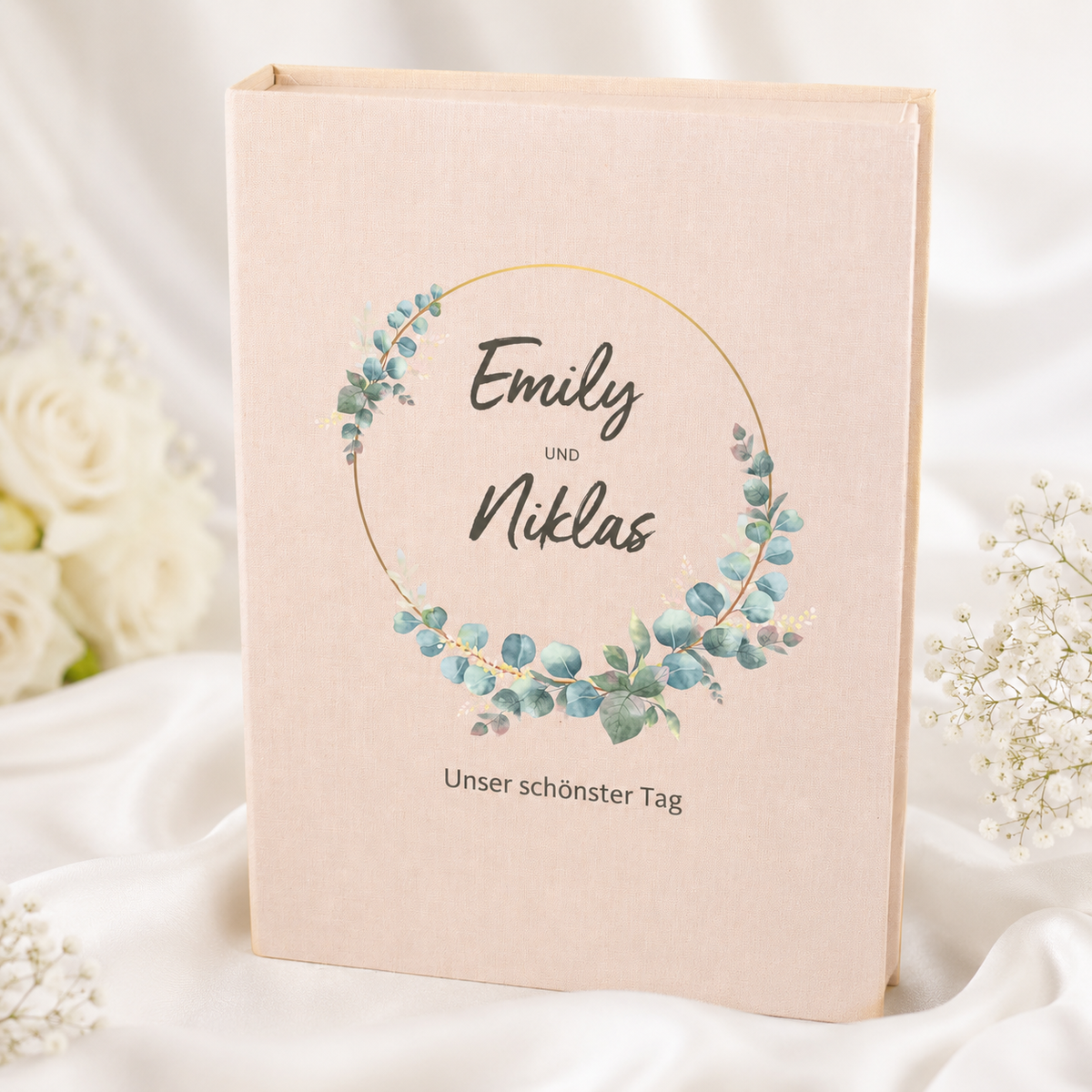 Beige Hochzeits-Erinnerungsbox in Buchform mit Eukalyptus-Motiv, personalisierten Namen und Wunschtext zwischen weißen Blumen