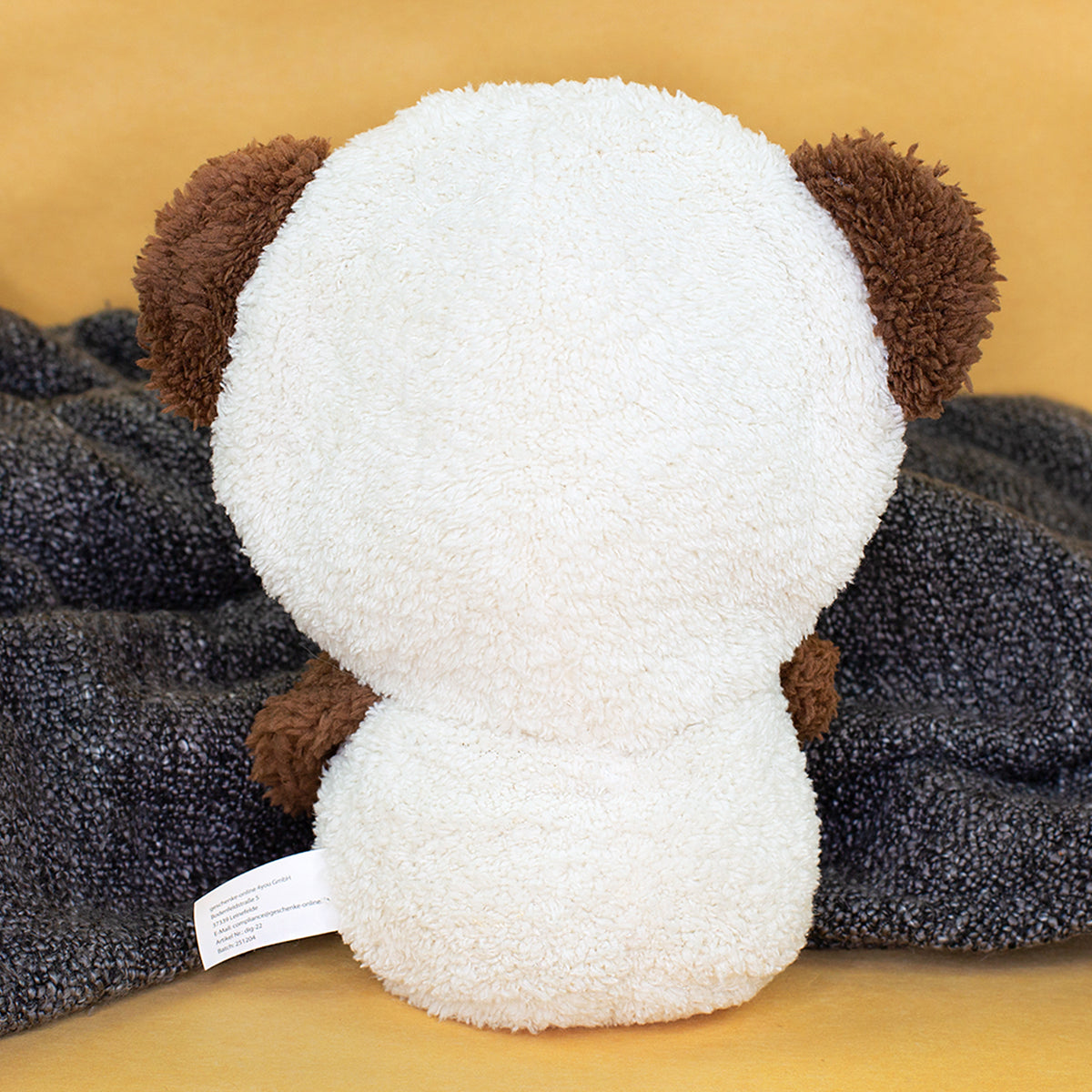 Rückansicht des cremeweißen Teddy-Kuscheltieres mit braunen Ohren auf grauer Decke
