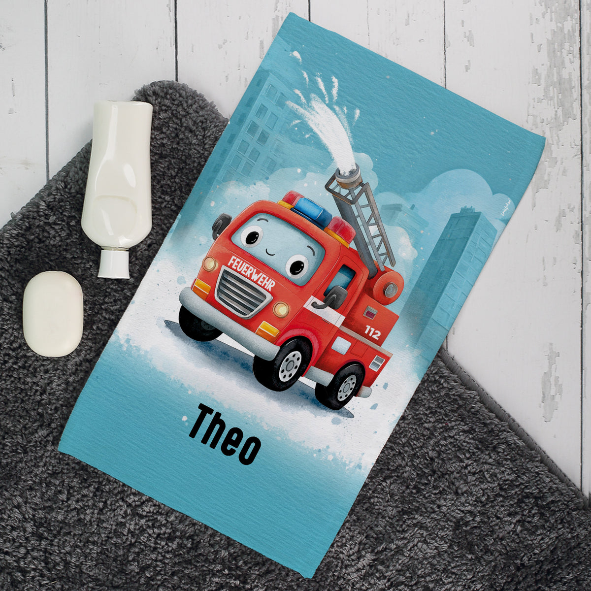 Personalisiertes Kinderhandtuch mit Feuerwehrauto Motiv und Name Theo auf grauem Badteppich