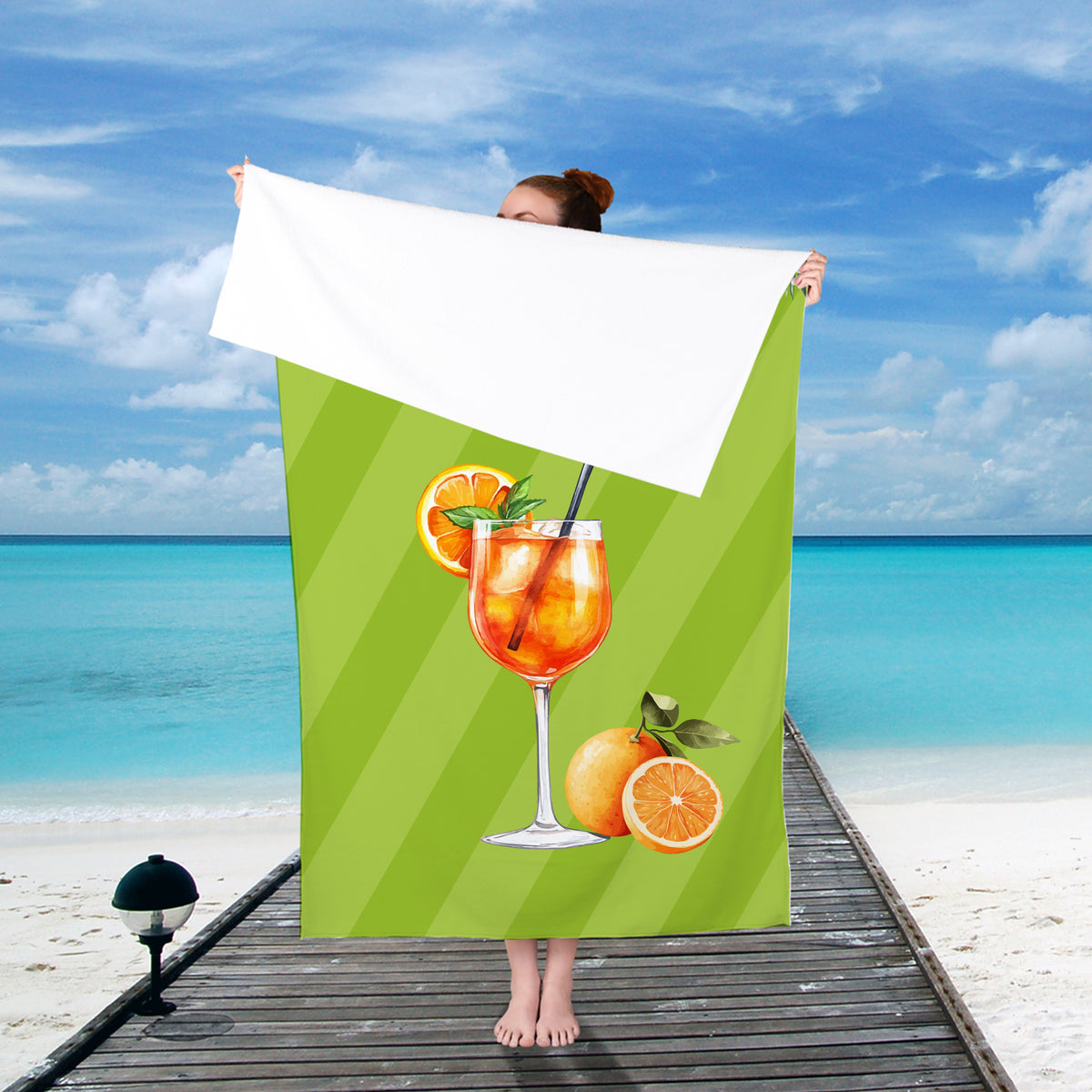 Frau hält ein personalisiertes Badetuch mit Aperol-Motiv und Wunschtext am Strand in die Höhe vor sonniger Kulisse.
