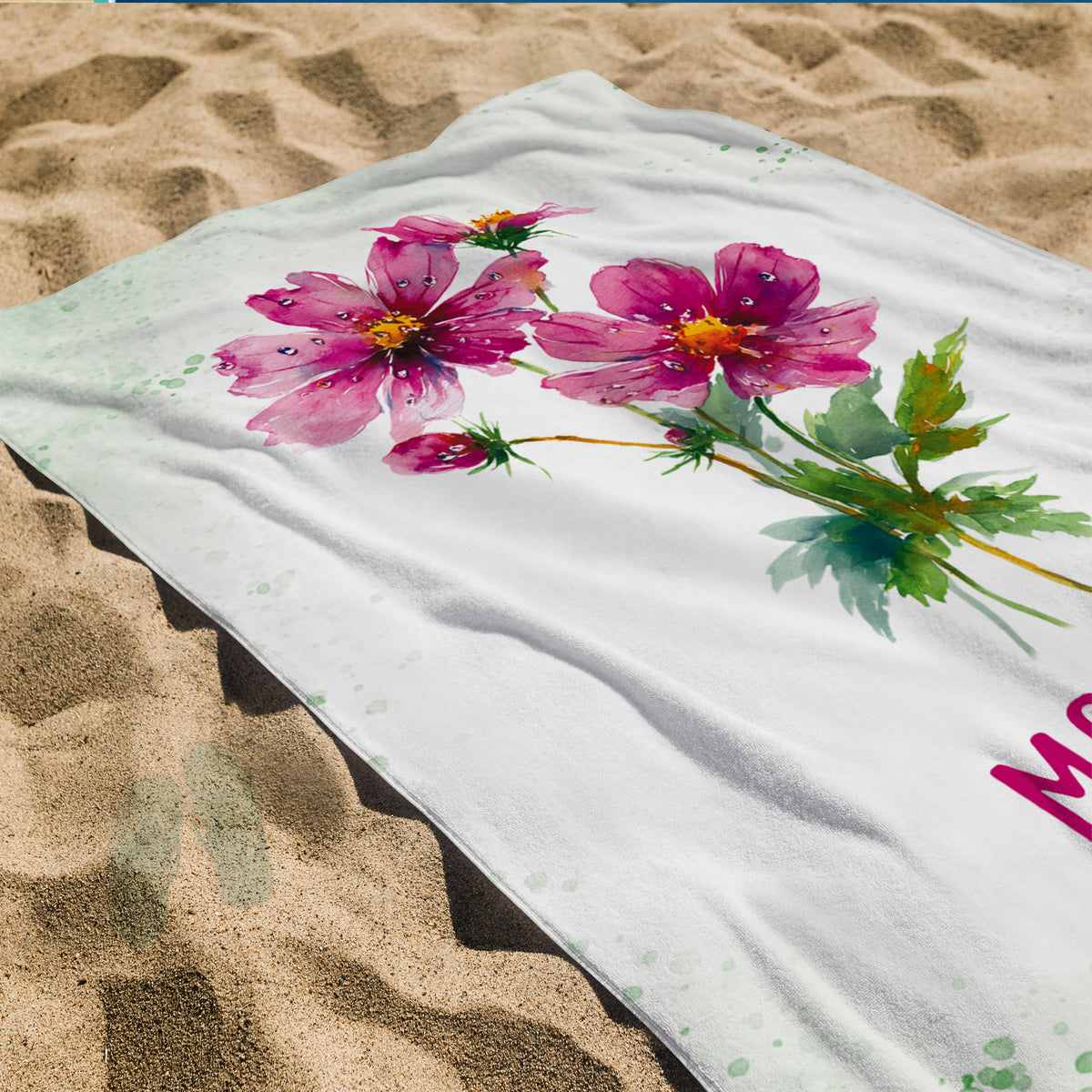 Badetuch mit rosa Blüten-Geburtsblume und Namensdruck auf Sandstrand als Detailansicht