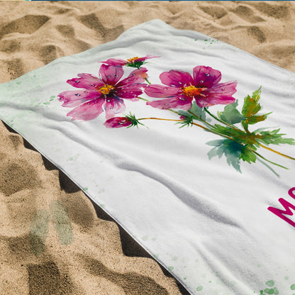 Badetuch mit rosa Blüten-Geburtsblume und Namensdruck auf Sandstrand als Detailansicht