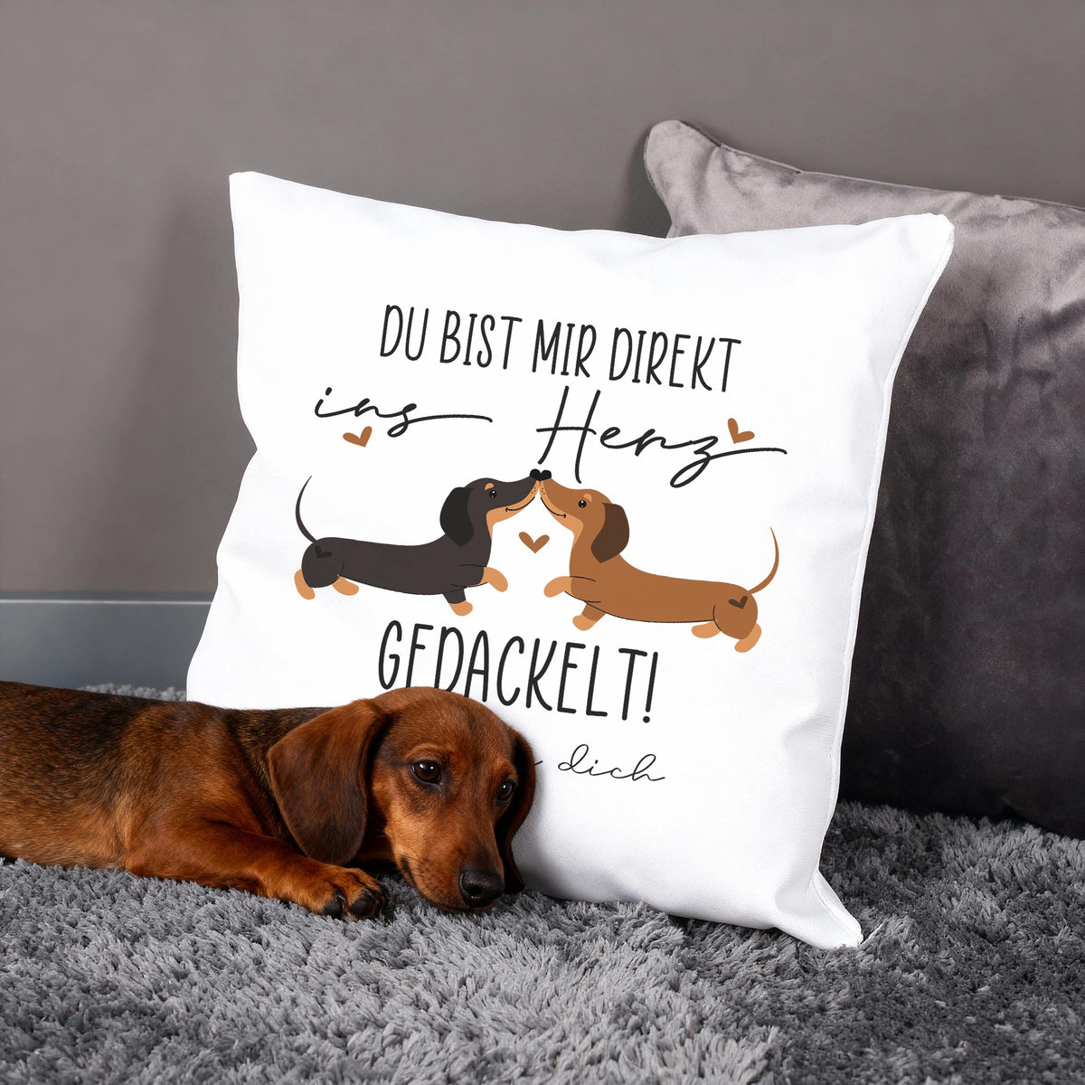 Personalisiertes Kissen mit Dackel-Pärchen und Spruch „Du bist mir direkt ins Herz gedackelt!“, Hund liegt davor