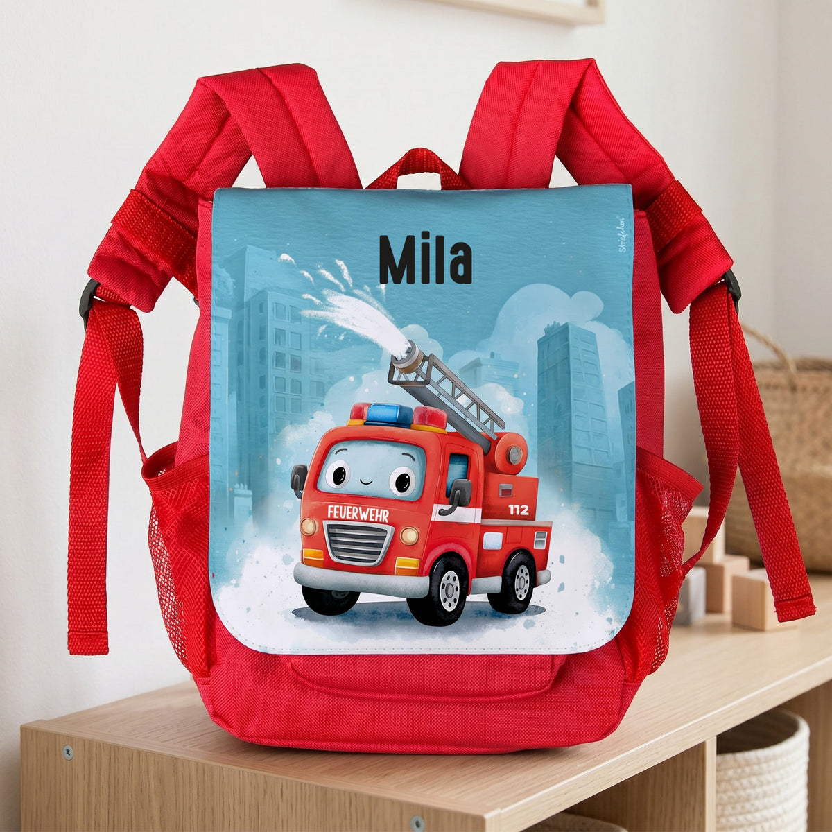 Roter Kinderrucksack mit Feuerwehr-Motiv und Name Mila auf einem Regal im Kinderzimmer