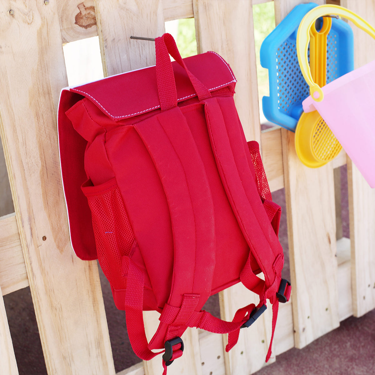 Rückansicht eines roten Kindergartenrucksacks mit gepolsterten Trageriemen an einer Holzwand