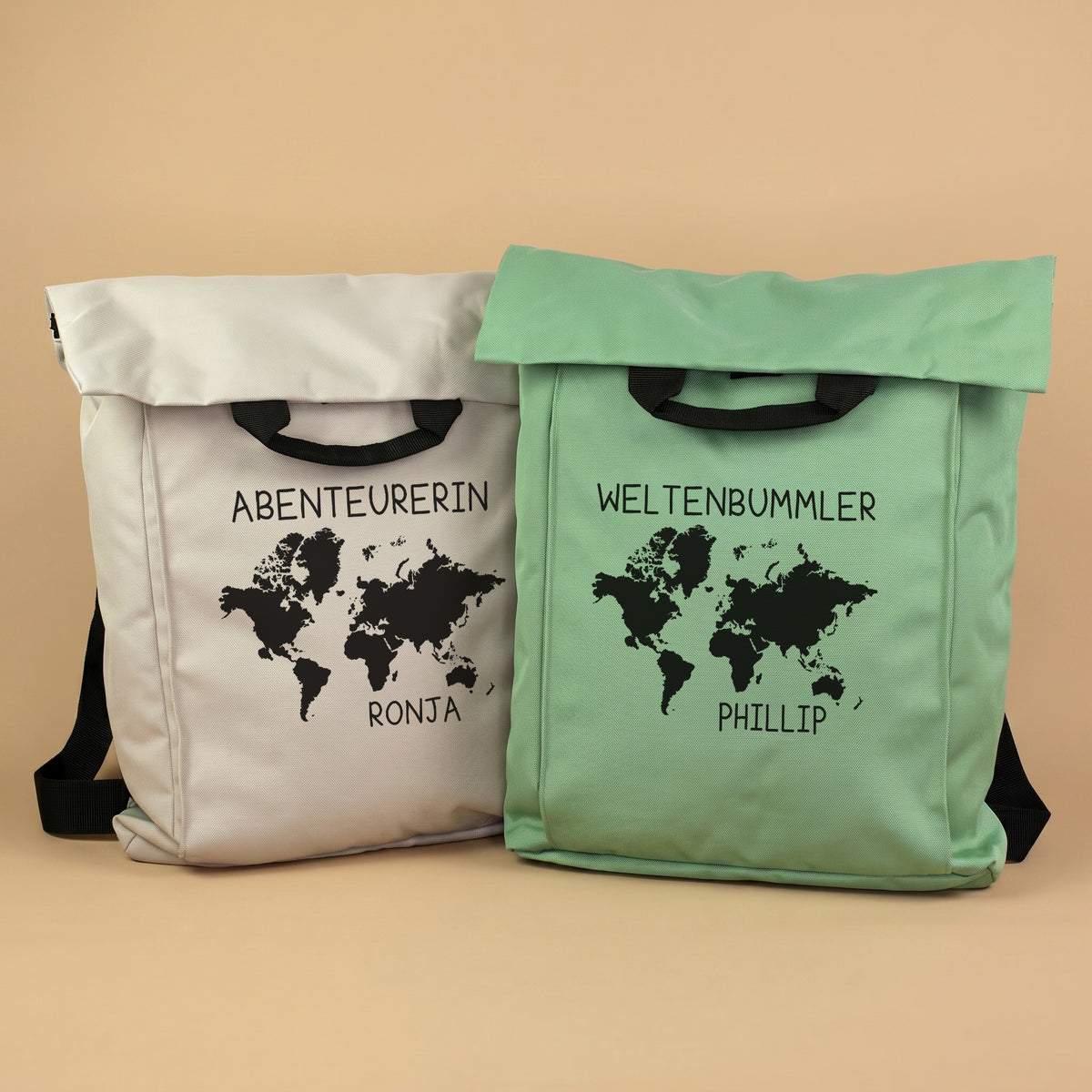 Zwei 2-in-1 Rucksäcke in Beige und Mintgrün mit Weltkarten-Motiv sowie personalisiertem Wunschtext und Namen vor hellem Hintergrund