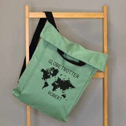 Jadegrüner 2-in-1 Rucksack mit Weltkarten-Motiv, Wunschtext „Globetrotter“ und Name „Robert“ an einer Holzleiter aufgehängt