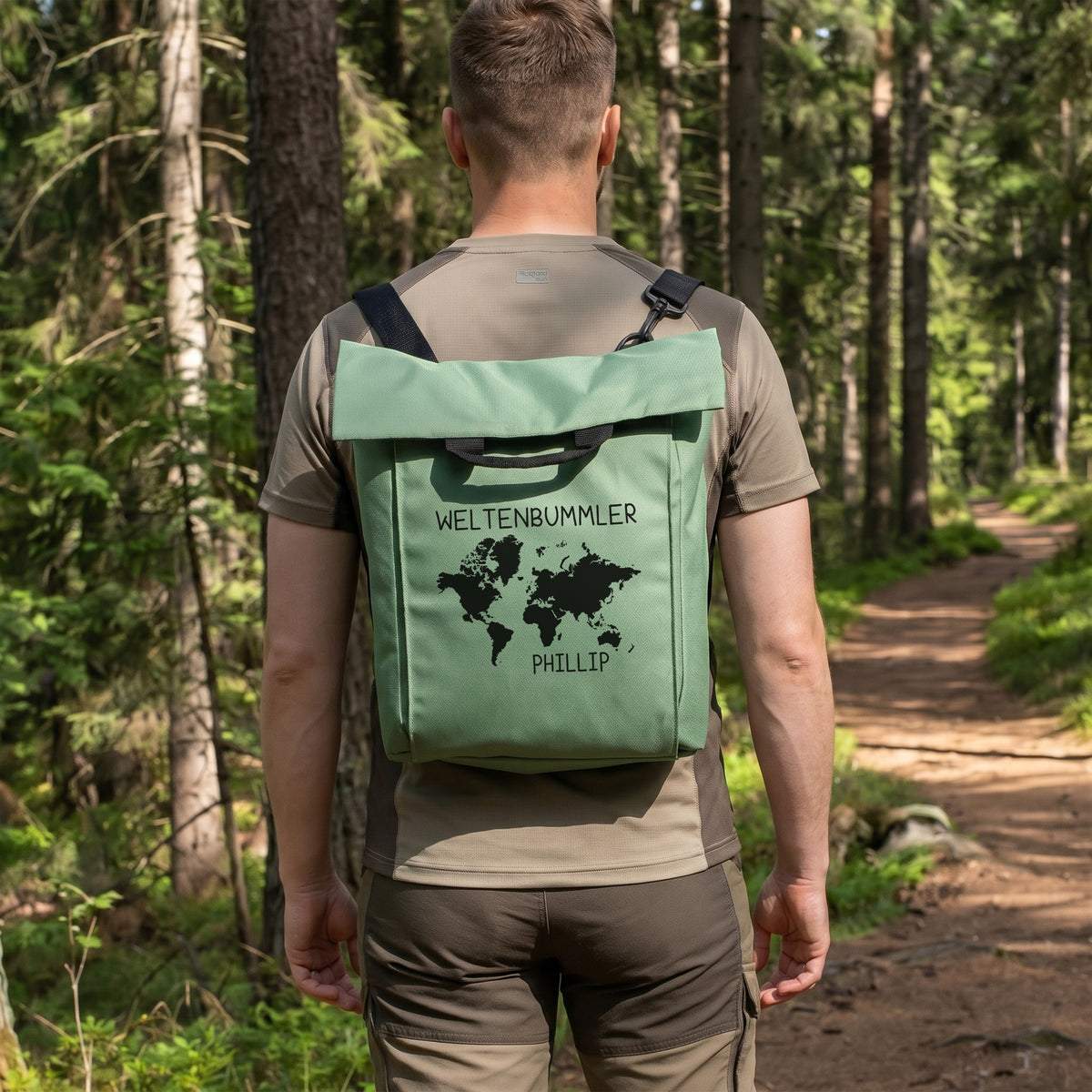 Mann trägt mintgrünen personalisierten 2-in-1 Rucksack mit Weltkarten-Motiv, Wunschtext „Weltenbummler“ und Name „Phillip“ im Wald