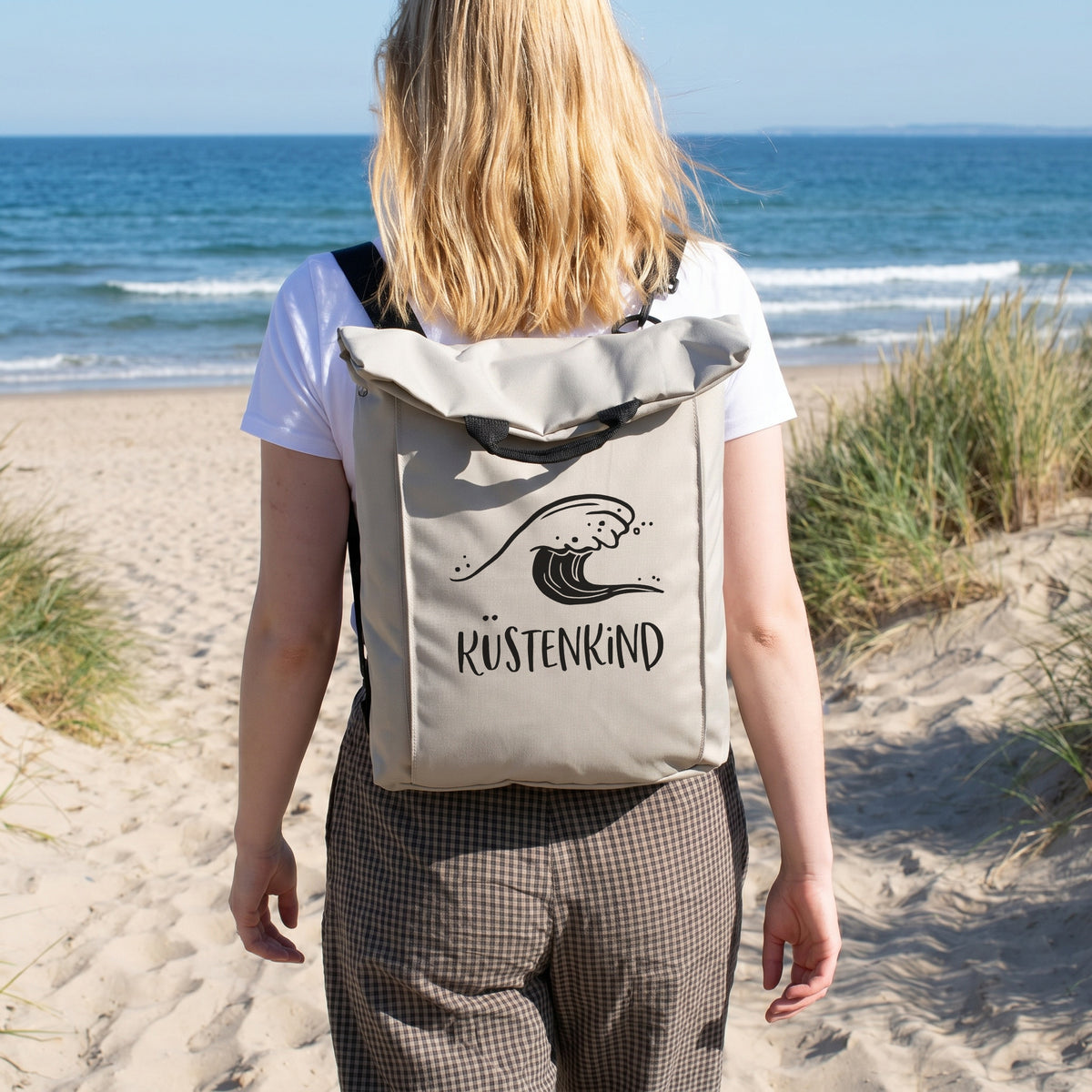 Beiger Rucksack mit Wellenmotiv und Wunschtext Küstenkind am Strand getragen