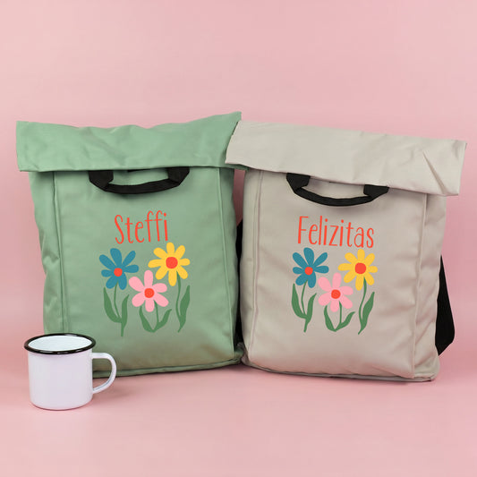 Zwei leichte 2-in-1 Rucksäcke in Jadegrün und Beige mit buntem Blumenmotiv und personalisiertem Namen, dekoriert mit weißer Tasse
