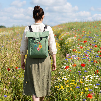 Personalisierter jadegrüner Blumen Rucksack mit Name Steffi auf dem Rücken einer Frau in einer bunten Blumenwiese