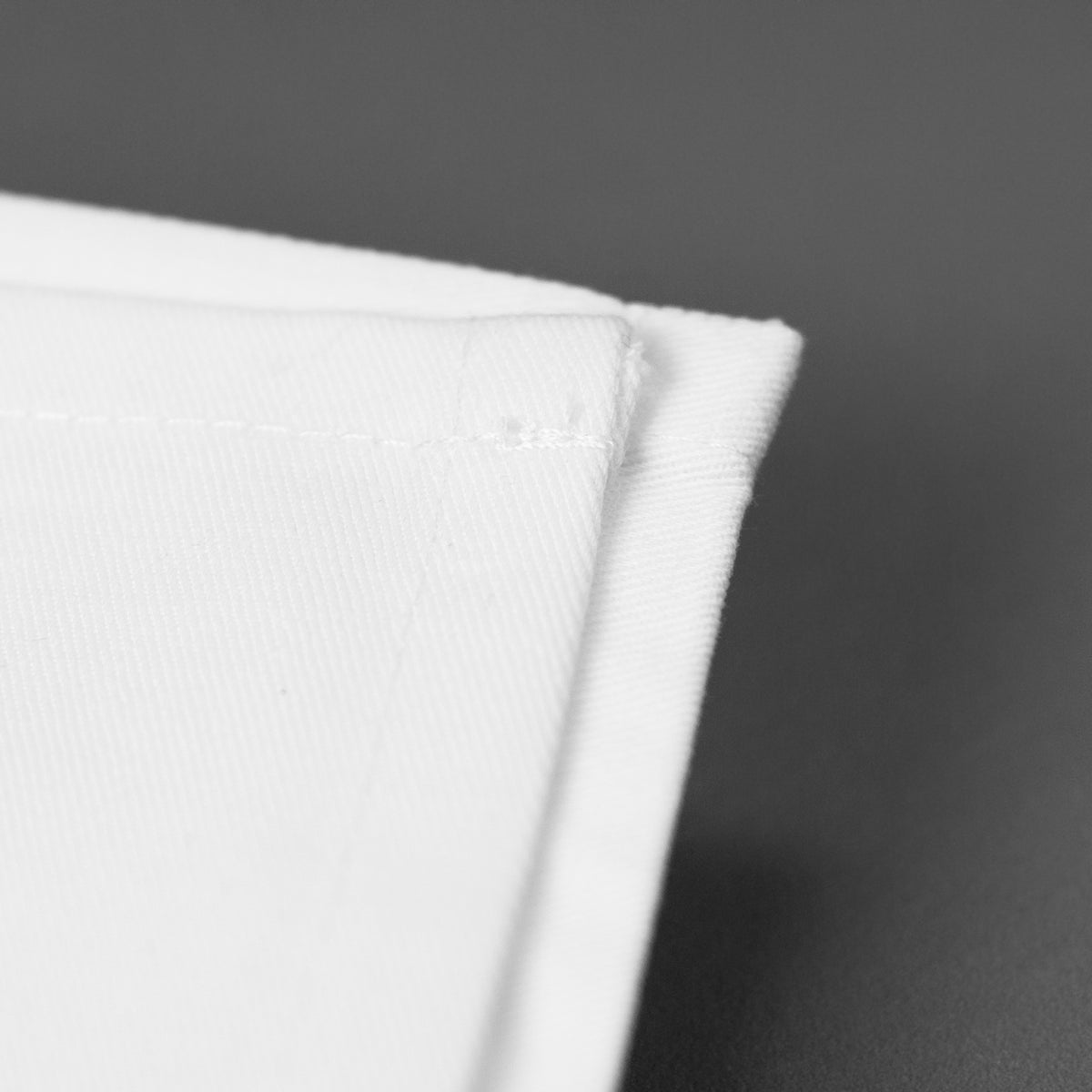 Detailaufnahme der hochwertigen Stoffkante einer weißen Serviette