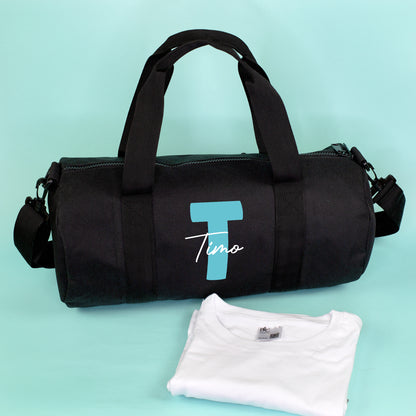 Schwarze Sporttasche mit türkiser Initiale T und Name Timo, dekoriert mit weißem Shirt vor türkisfarbenem Hintergrund