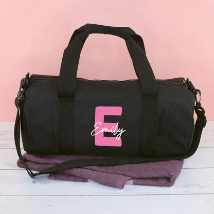 Schwarze Sporttasche mit pinker Initiale E und Name Emily, als personalisierte Trainingstasche vor rosa Hintergrund