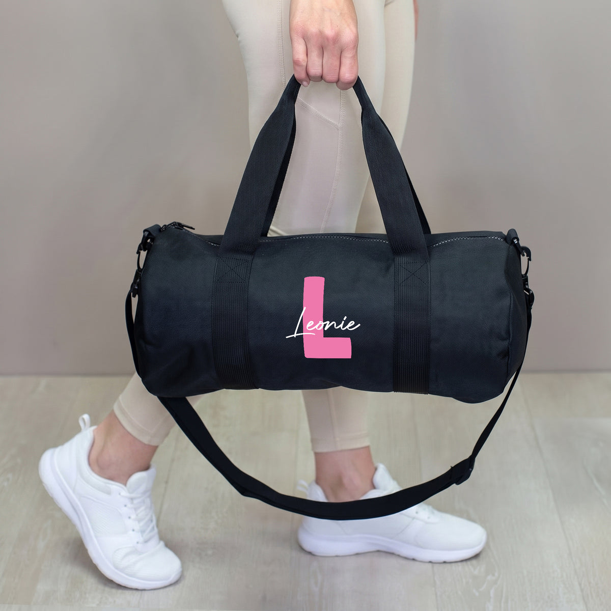 Schwarze Sporttasche mit pinker Initiale L und Name Leonie, getragen in der Hand mit Schultergurt