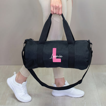 Schwarze Sporttasche mit pinker Initiale L und Name Leonie, getragen in der Hand mit Schultergurt